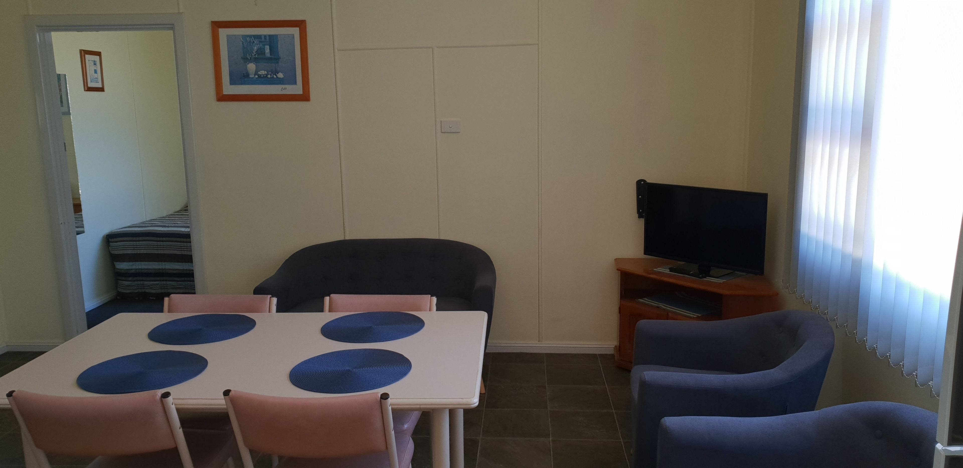 Una habitación con una mesa de comedor, sillas, un televisor sobre un mueble bajo y una ventana con persianas.
