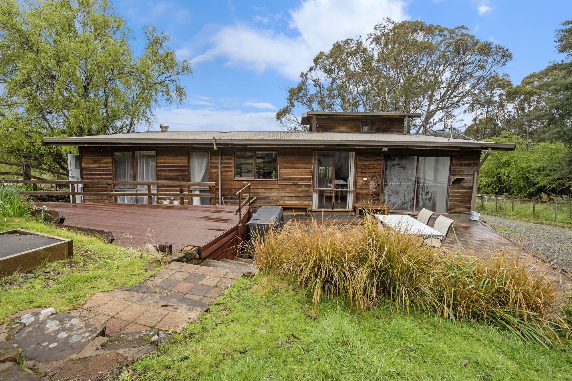 A wooden cabin with a deck, surrounded by grass and trees.
