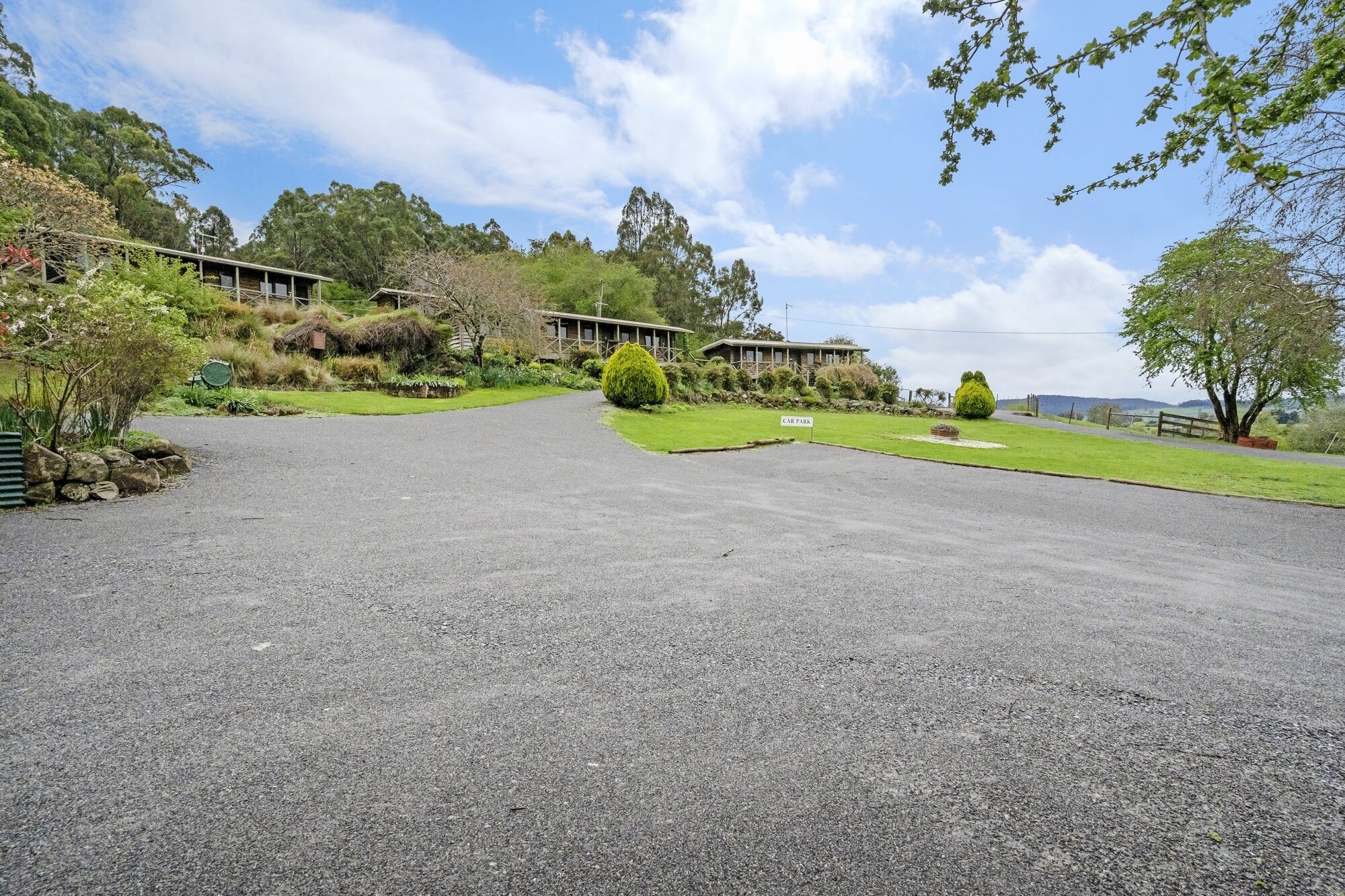 A gravel driveway leading to a building with a car park sign.