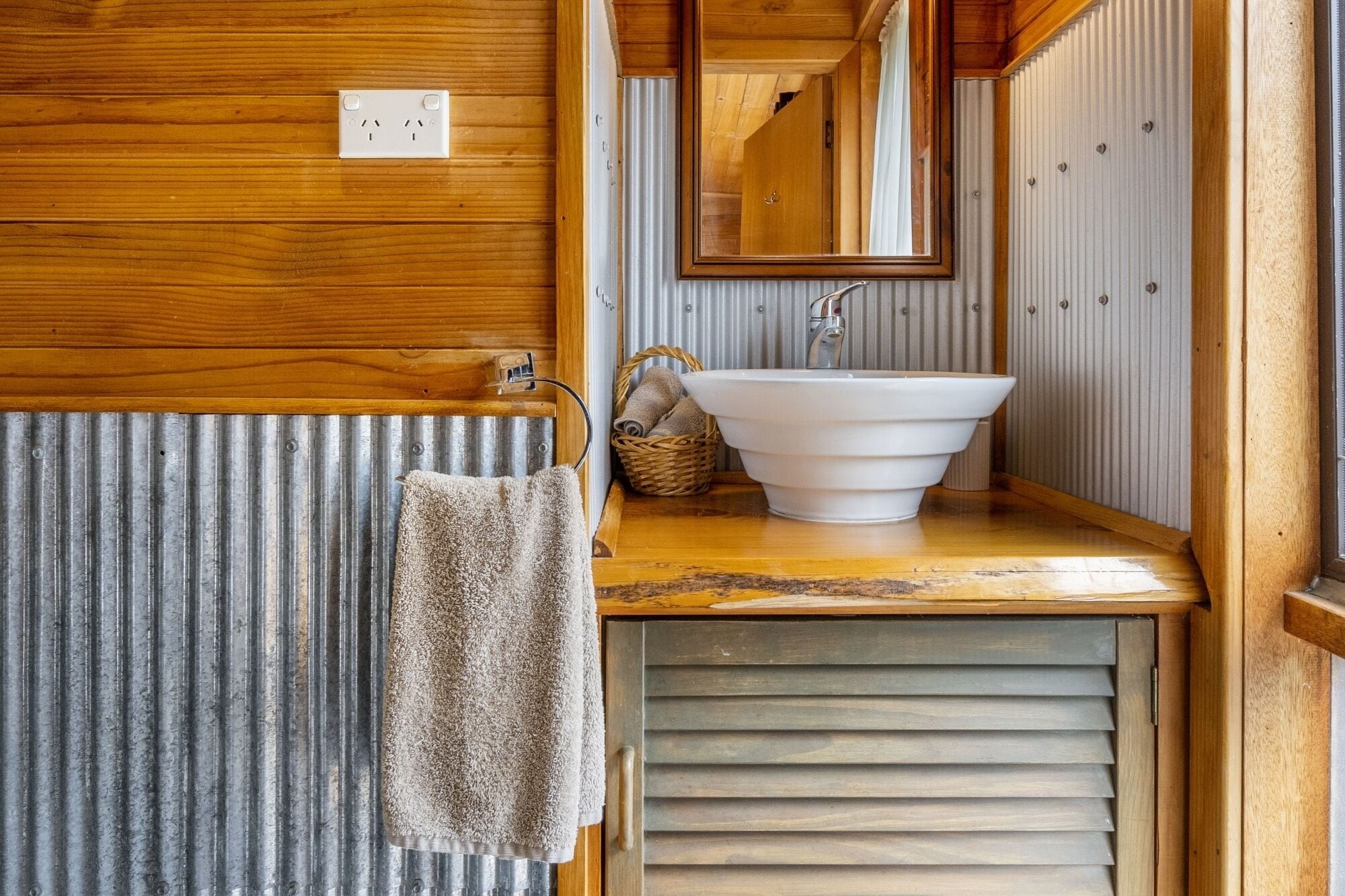 A bathroom with a wooden vanity, a white sink, a towel hanging on a rack, and a mirror.