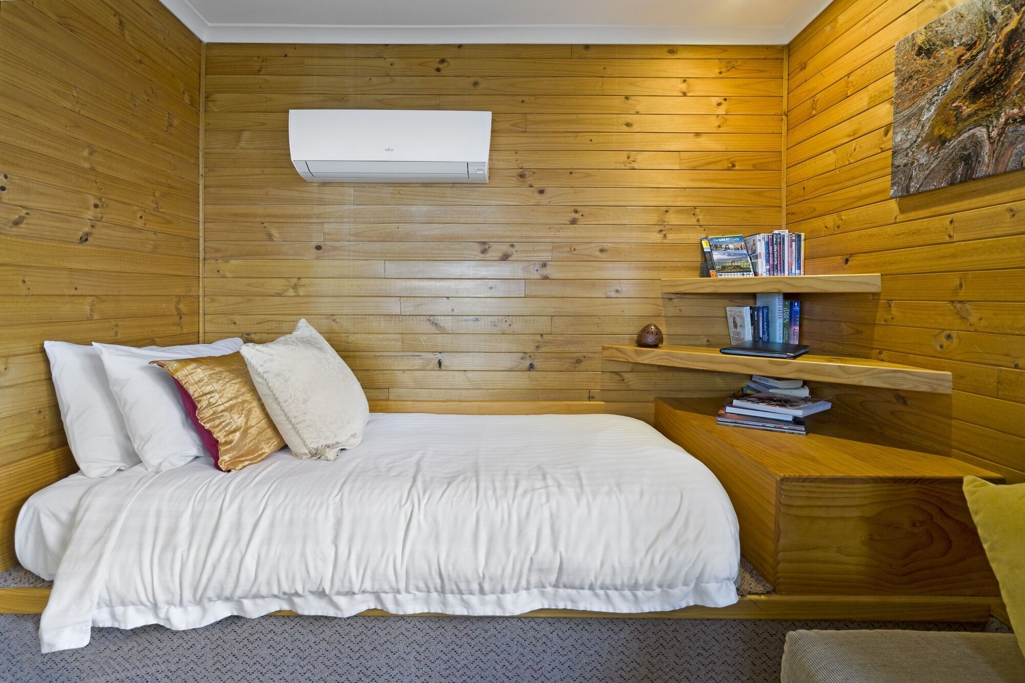 A wooden-paneled room with a bed, white bedding, a bookshelf, and an air conditioning unit.