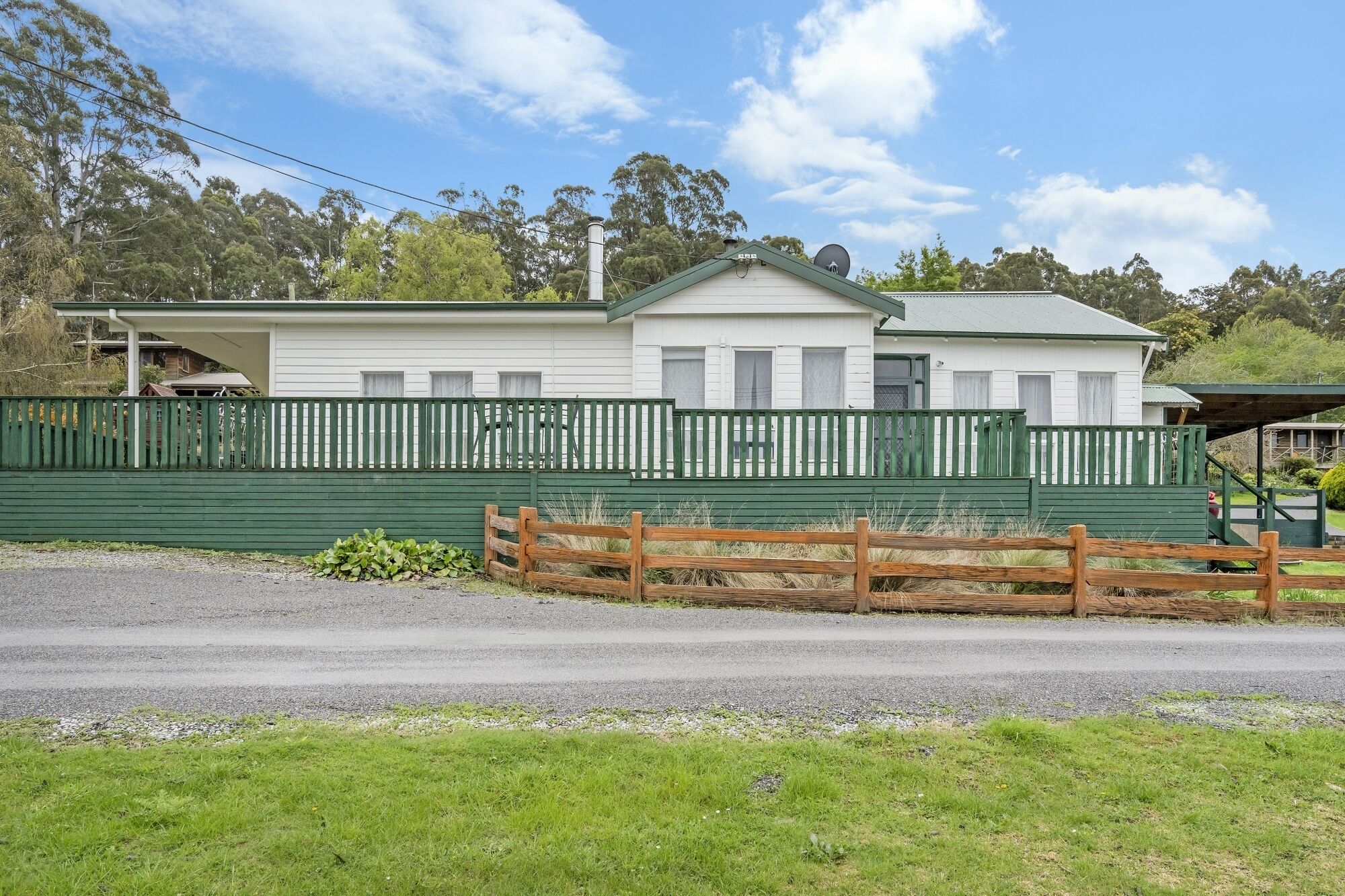A two-story white building with a green roof and white trim, surrounded by a green fence.