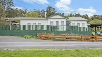 A two-story white building with a green roof and white trim, surrounded by a green fence.