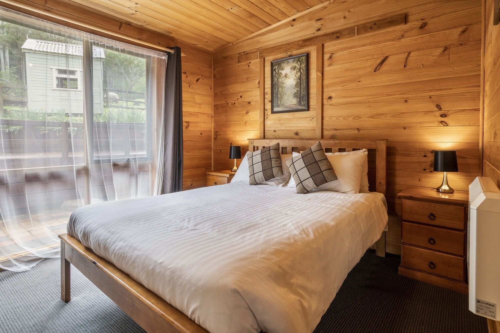 A wooden-paneled bedroom with a large bed, two bedside tables, and a window with curtains.