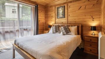 A wooden-paneled bedroom with a large bed, two bedside tables, and a window with curtains.