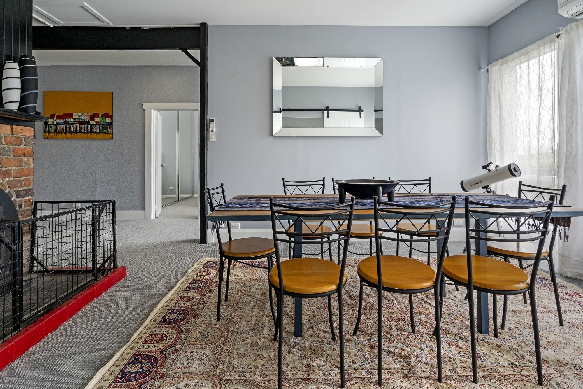 Un comedor con una mesa y sillas, un espejo grande en la pared y un telescopio sobre un soporte.