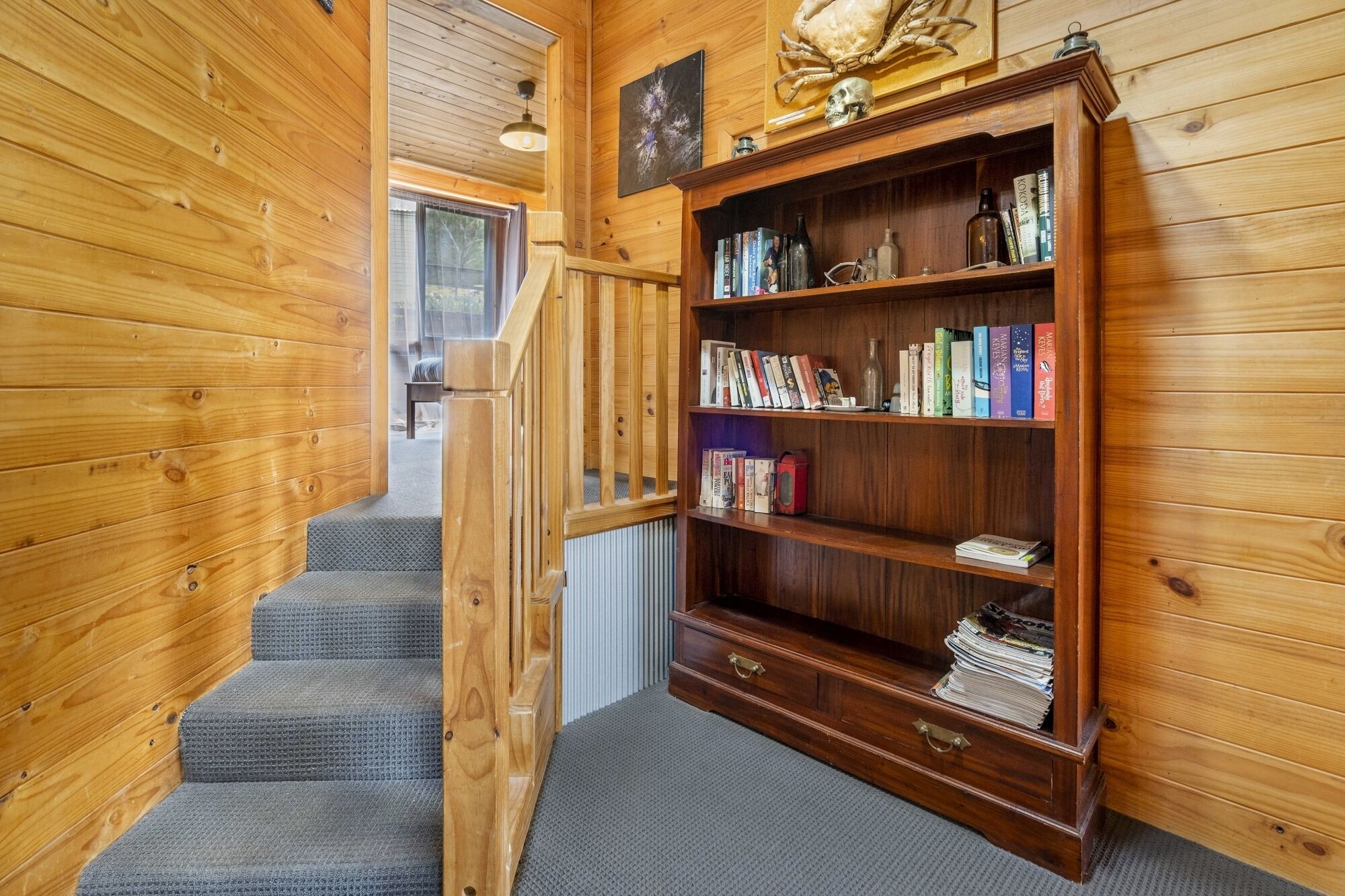 A wooden interior with a bookshelf, a staircase, and a window.