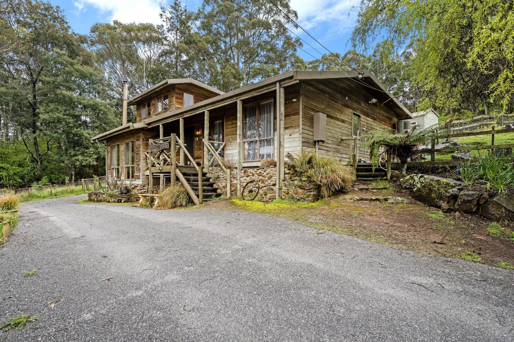 A rustic wooden lodge with a porch, stone steps, and a gravel driveway.