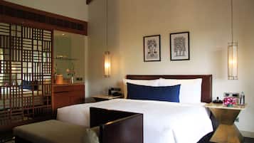 A hotel room with a large bed, a wooden headboard, a bedside table with a lamp, a nightstand, and a decorative screen.