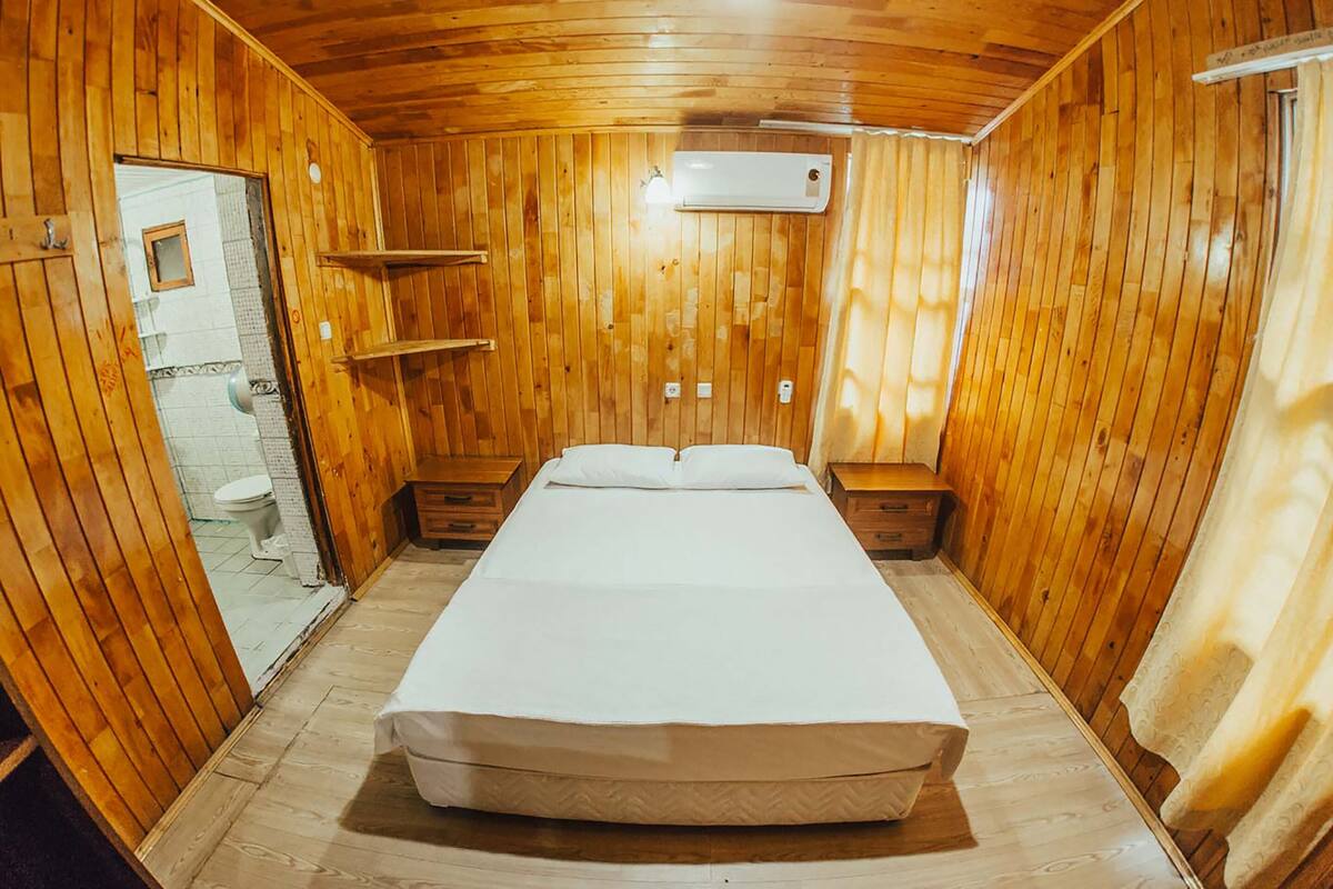 A wooden room with a bed, a toilet, and an air conditioning unit.