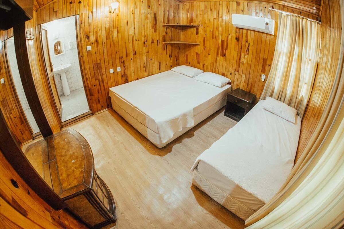 A wooden room with two beds, a small table, and a mirror.