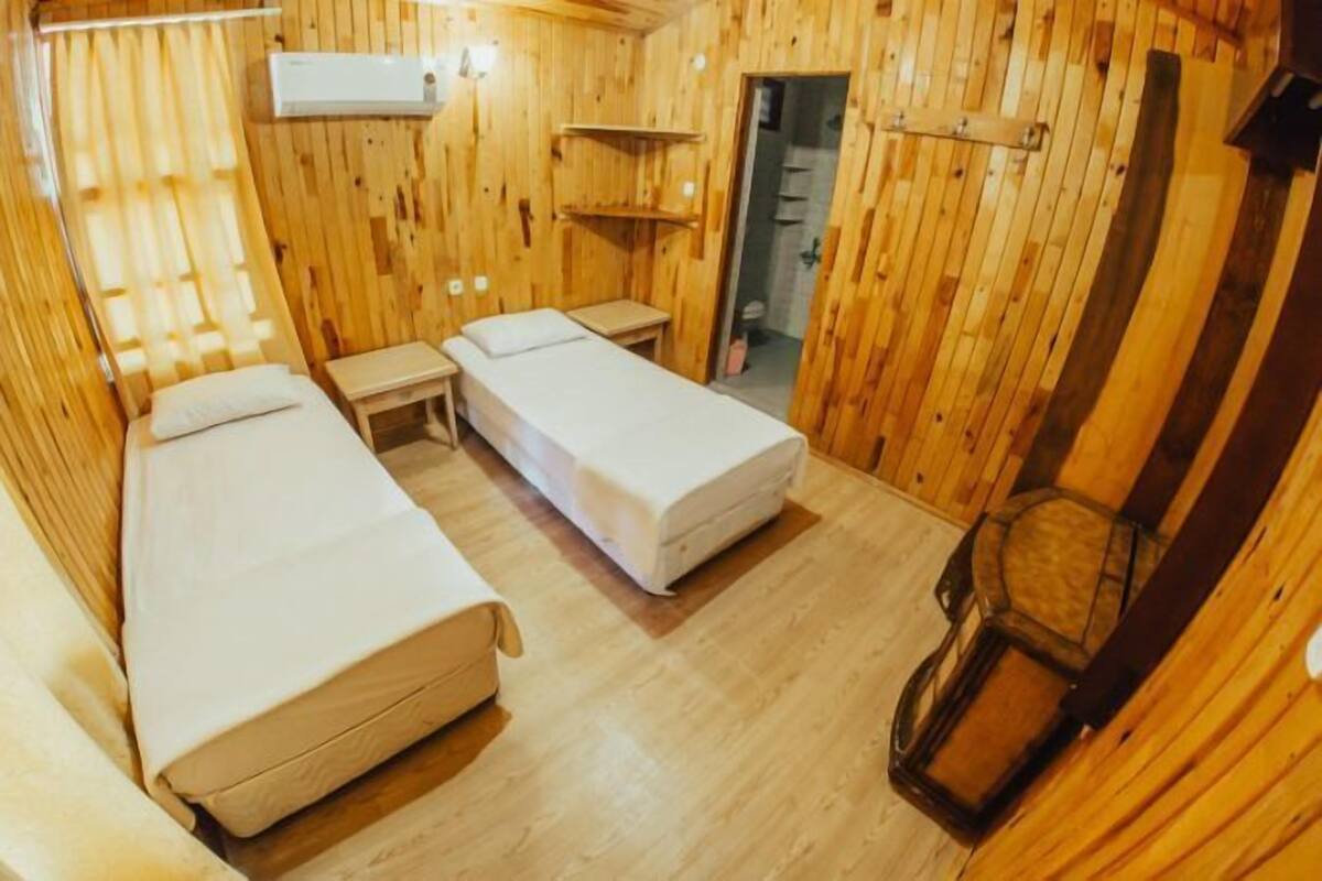 A wooden cabin room with two beds, a small table, and a shelf.