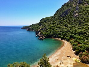 A coastal landscape with a beach, clear turquoise waters, and dense green vegetation on a hillside. - Kadir's Tree Houses (Kumluca)