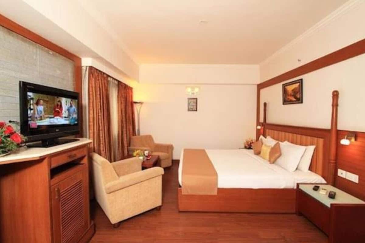 Quarto de hotel com cama, televisão, escrivaninha e cadeira.