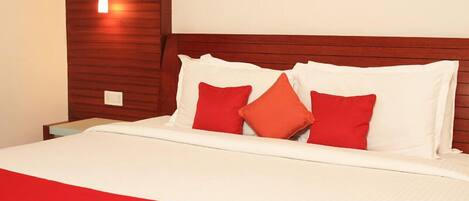 Uma cama bem arrumada com roupa de cama branca e vermelha, uma cabeceira de madeira e uma luminária fixada na parede.