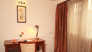 A hotel room with a wooden desk, a chair, a lamp, a framed picture, and a window with curtains. -  Parijatha Gateway (Bengaluru)