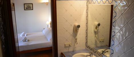 Habitació d'hotel amb un llit, un bany amb un rentatge i un mirall, i un suport per tovalloles.