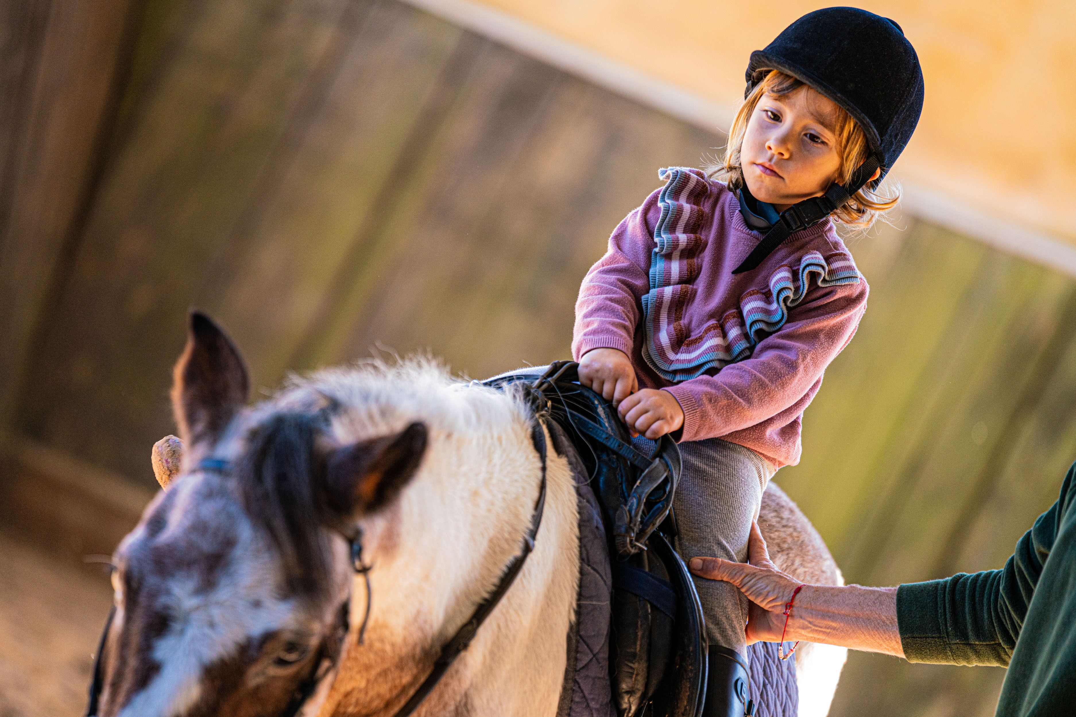 A child riding a horse in an indoor setting with wooden walls.