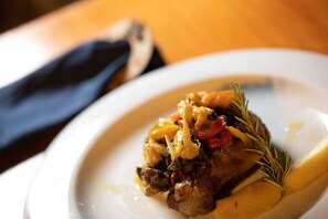 A plate of food with a piece of meat, vegetables, and a sprig of rosemary. - Son Menut (Felanitx)