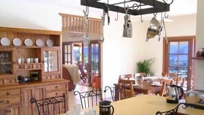 A dining area with a wooden table and chairs, a coffee pot, and a view through large windows. - The Summit Rainforest Retreat (Atherton)