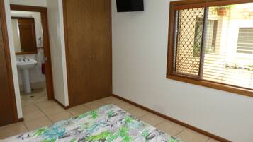 Ein Schlafzimmer mit Bett, Kleiderschrank, einem an der Wand montierten Fernseher und einem Fenster mit Blick nach draußen.