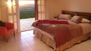 A bedroom with a large bed, a chair, and a view of the landscape through an open door. - The Summit Rainforest Retreat (Atherton)