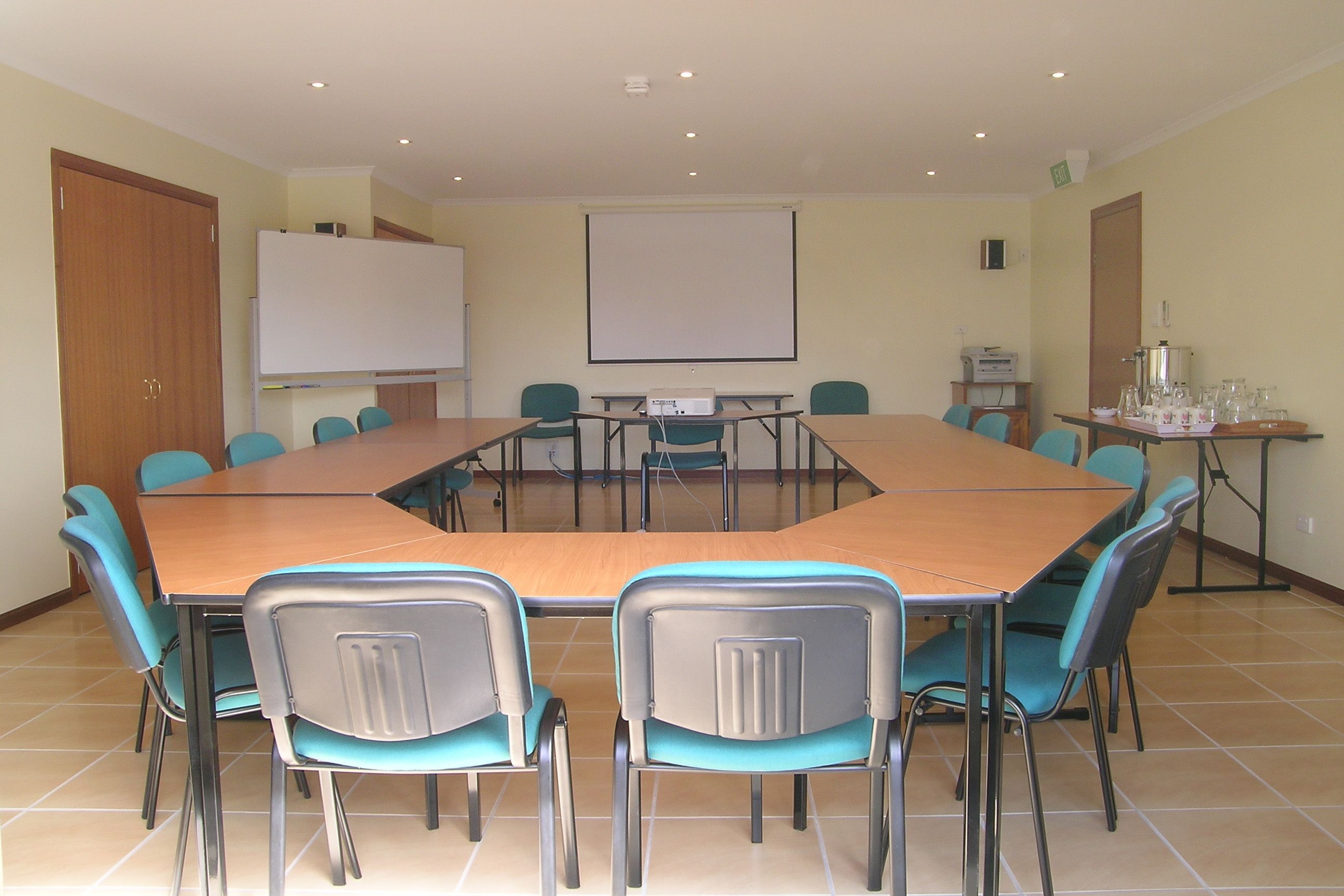 Un salón de conferencias con una larga mesa, sillas color turquesa, una pizarra y una pantalla para proyector.