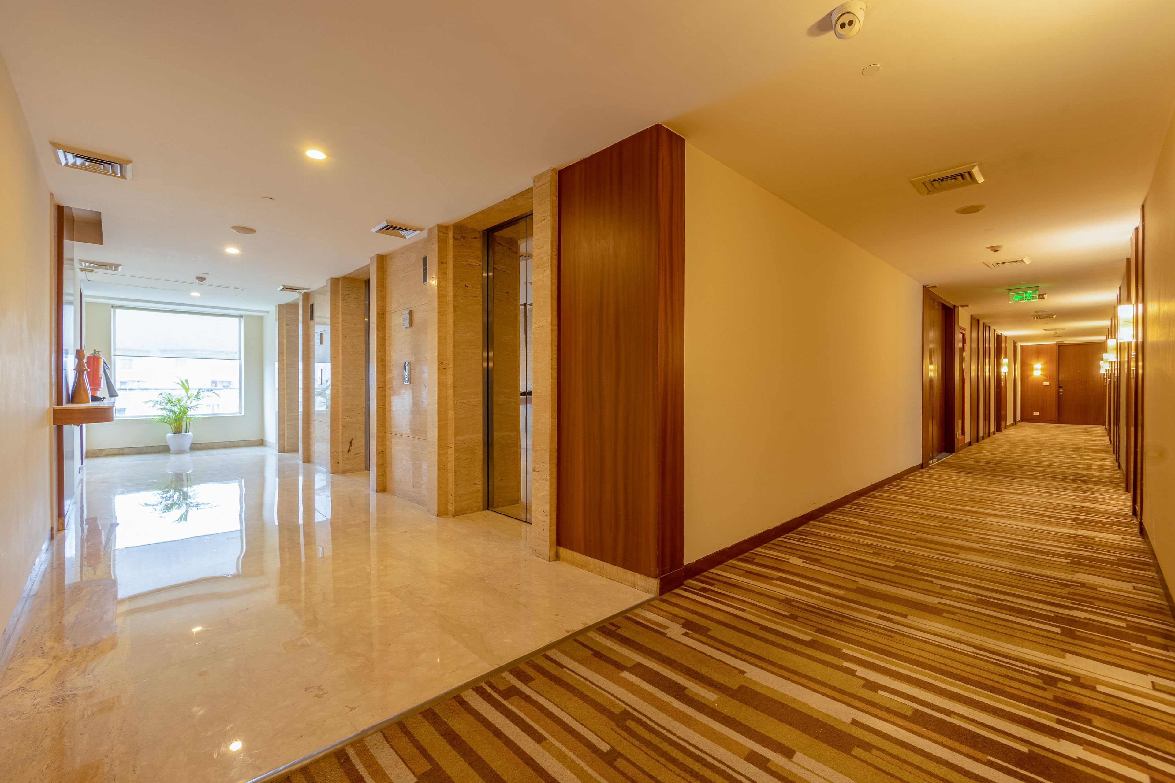 A hotel corridor with a shiny floor, wooden paneling, and a carpeted section.
