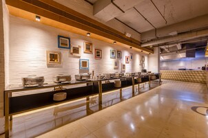 A buffet setup with multiple serving stations, a tiled floor, and a brick wall with framed pictures.