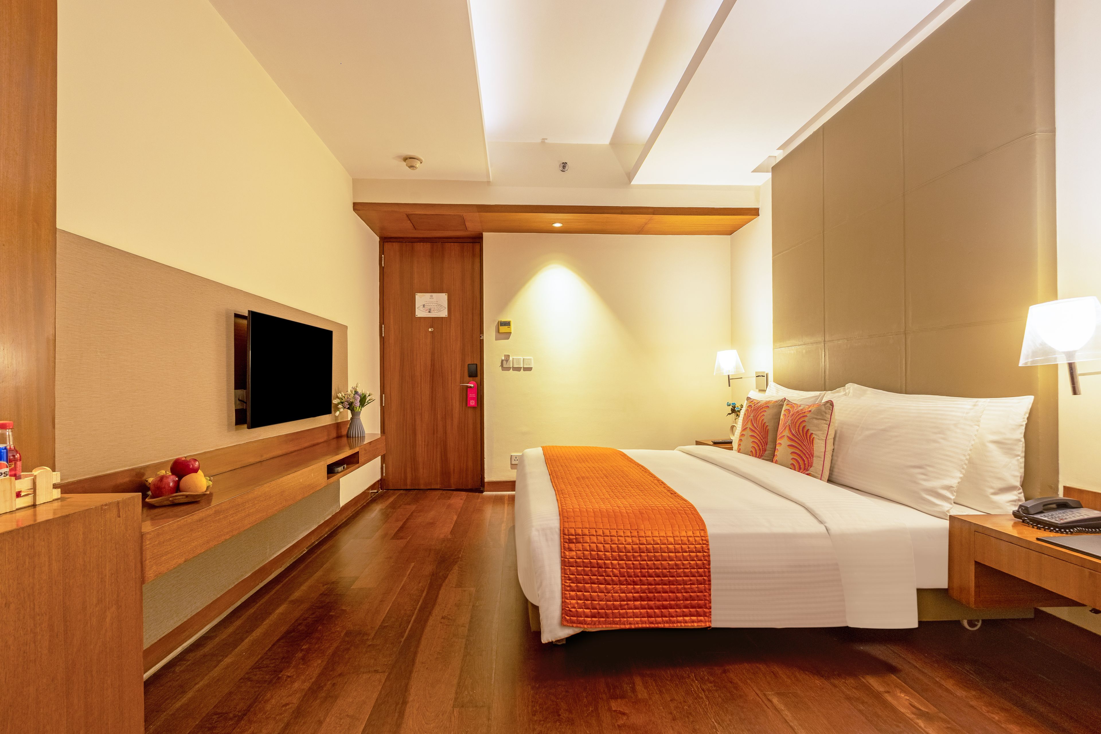 A hotel room with a bed, bedside table, lamp, and a flat-screen TV mounted on the wall.