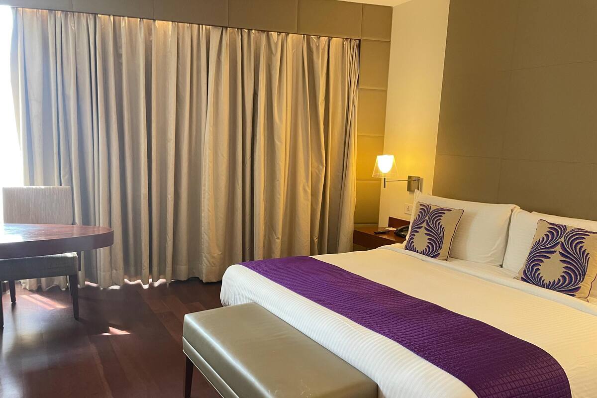 A hotel room with a bed, a bench, a desk, and a lamp.