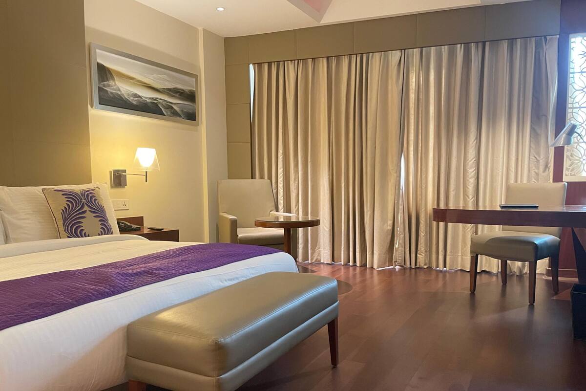 A hotel room with a large bed, a desk, a chair, and a window with curtains.