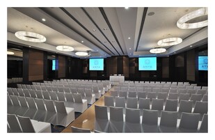 A conference room with rows of white chairs, a long table, and large screens displaying the 'ANYA' logo.