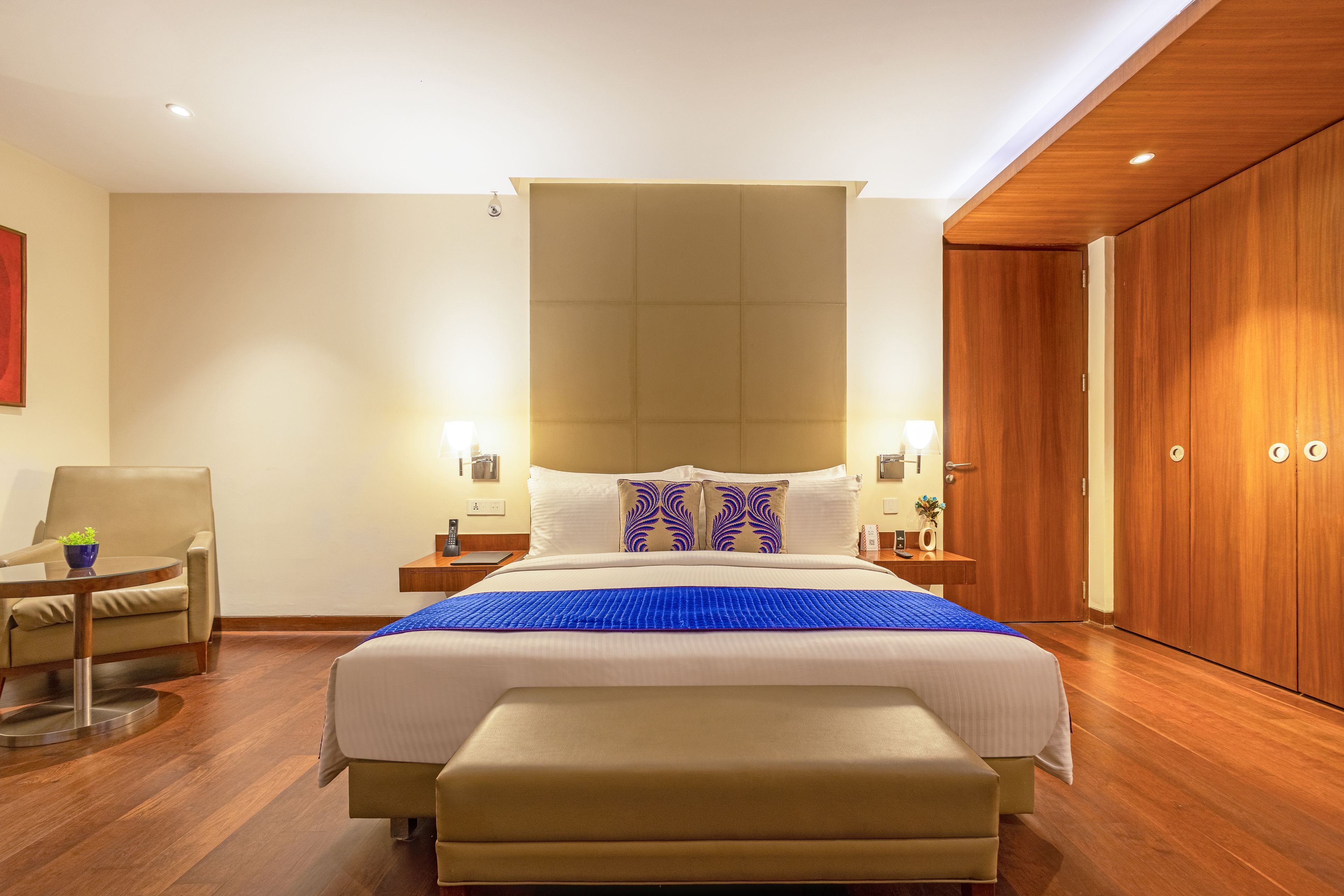 Habitación de hotel con una cama grande, un armario de madera, un escritorio con una silla y una mesita con una planta.