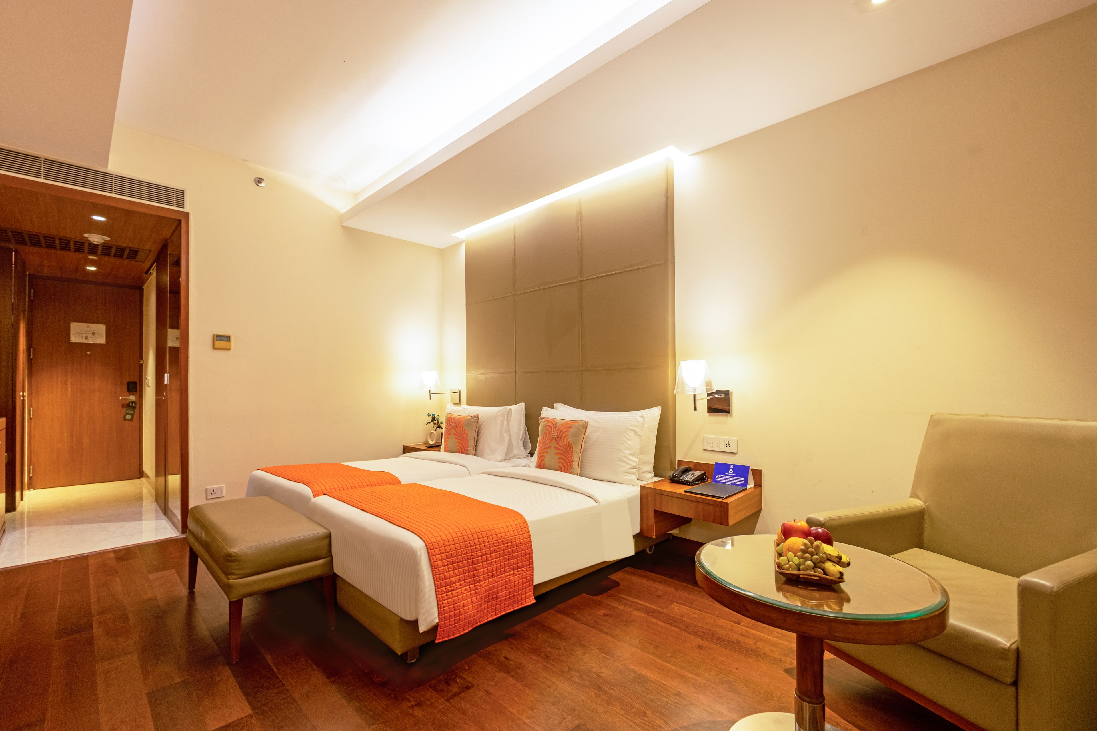 A hotel room with a bed, a desk, a chair, and a small table with fruit.