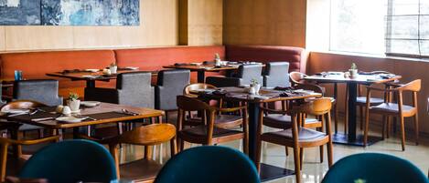 A restaurant with multiple tables and booths, wooden furniture, and a large abstract painting on the wall.