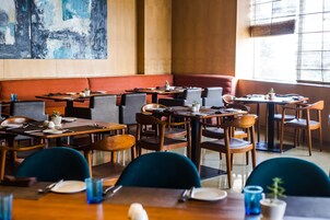 A restaurant with multiple tables and booths, wooden furniture, and a large abstract painting on the wall.