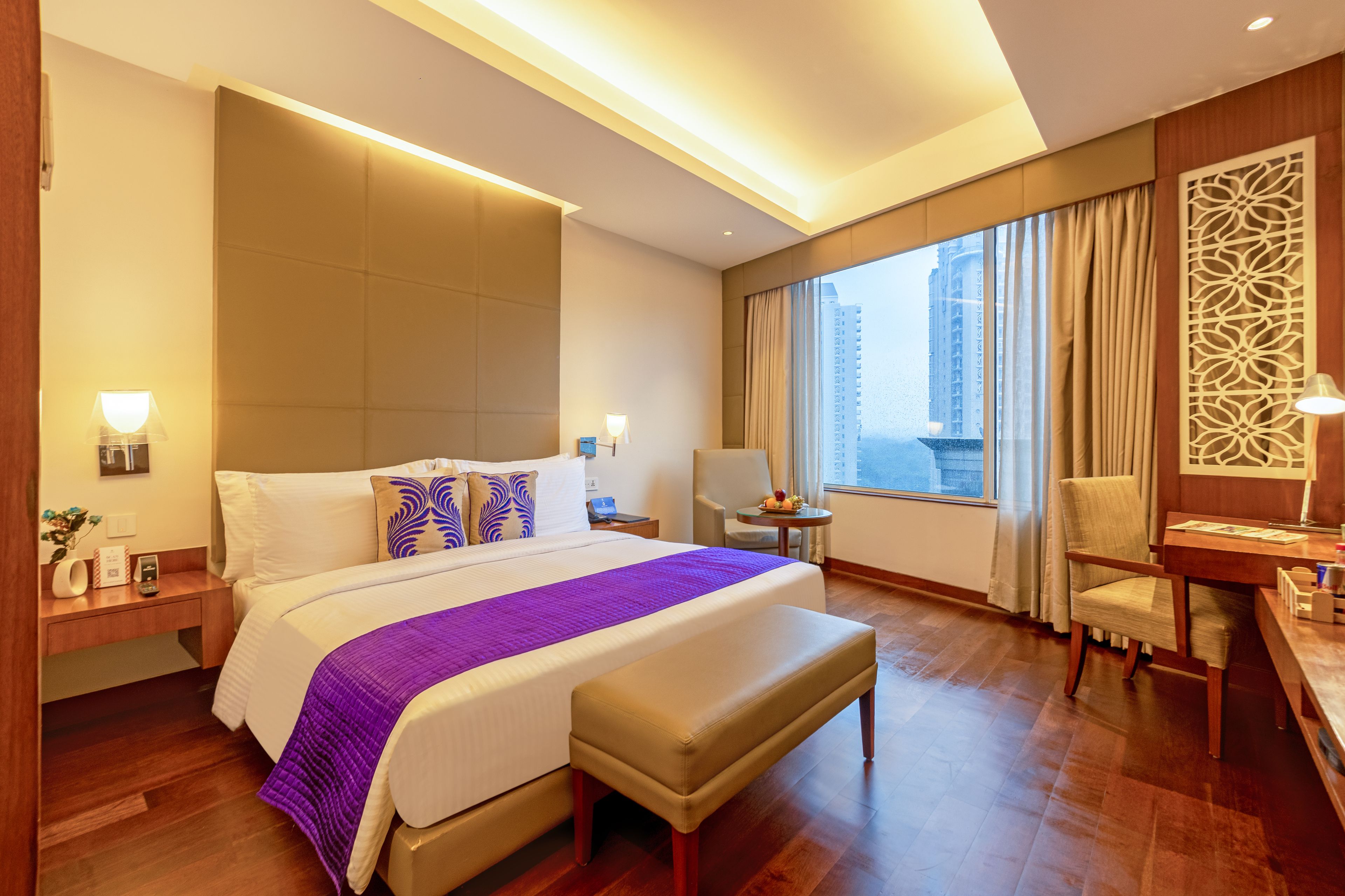 A hotel room with a large bed, a desk, a chair, and a view of the city.