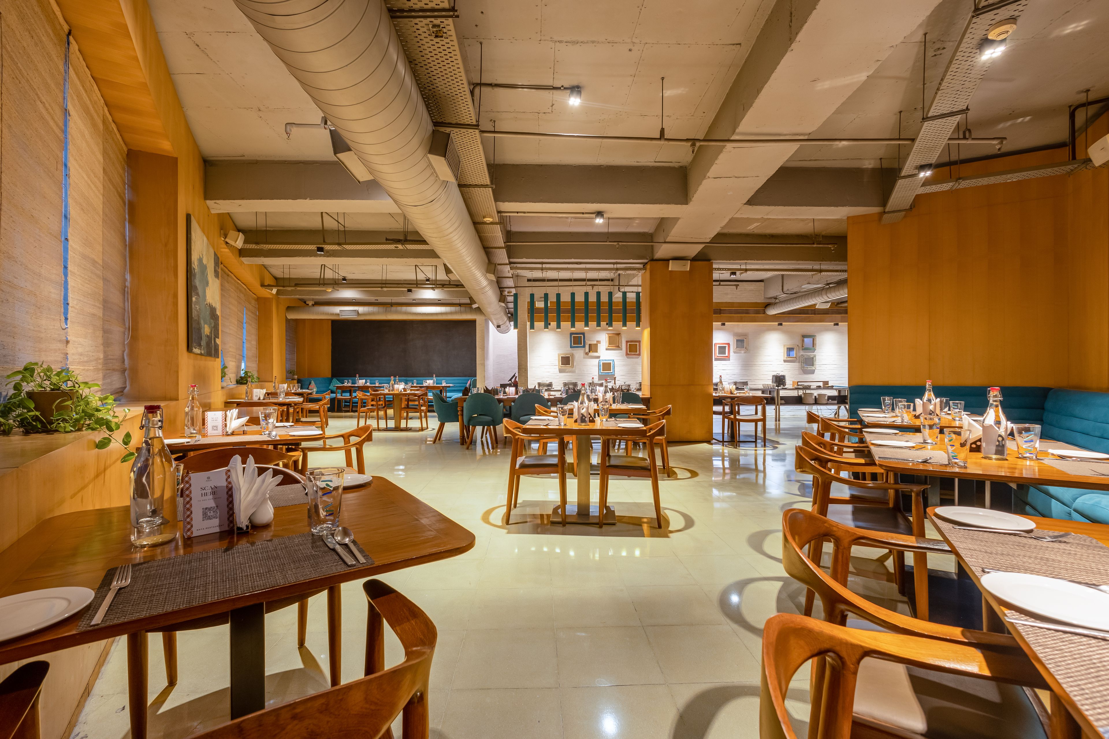 A spacious restaurant with wooden tables and chairs, a bar area, and a view of the kitchen.