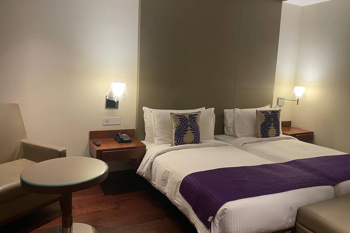 A hotel room with two beds, a small table, a chair, and a nightstand with a phone.