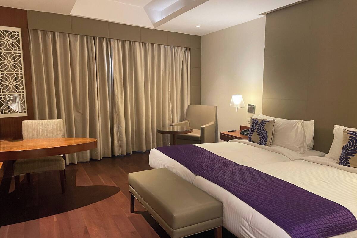 A hotel room with a large bed, a desk, a chair, and a small table.