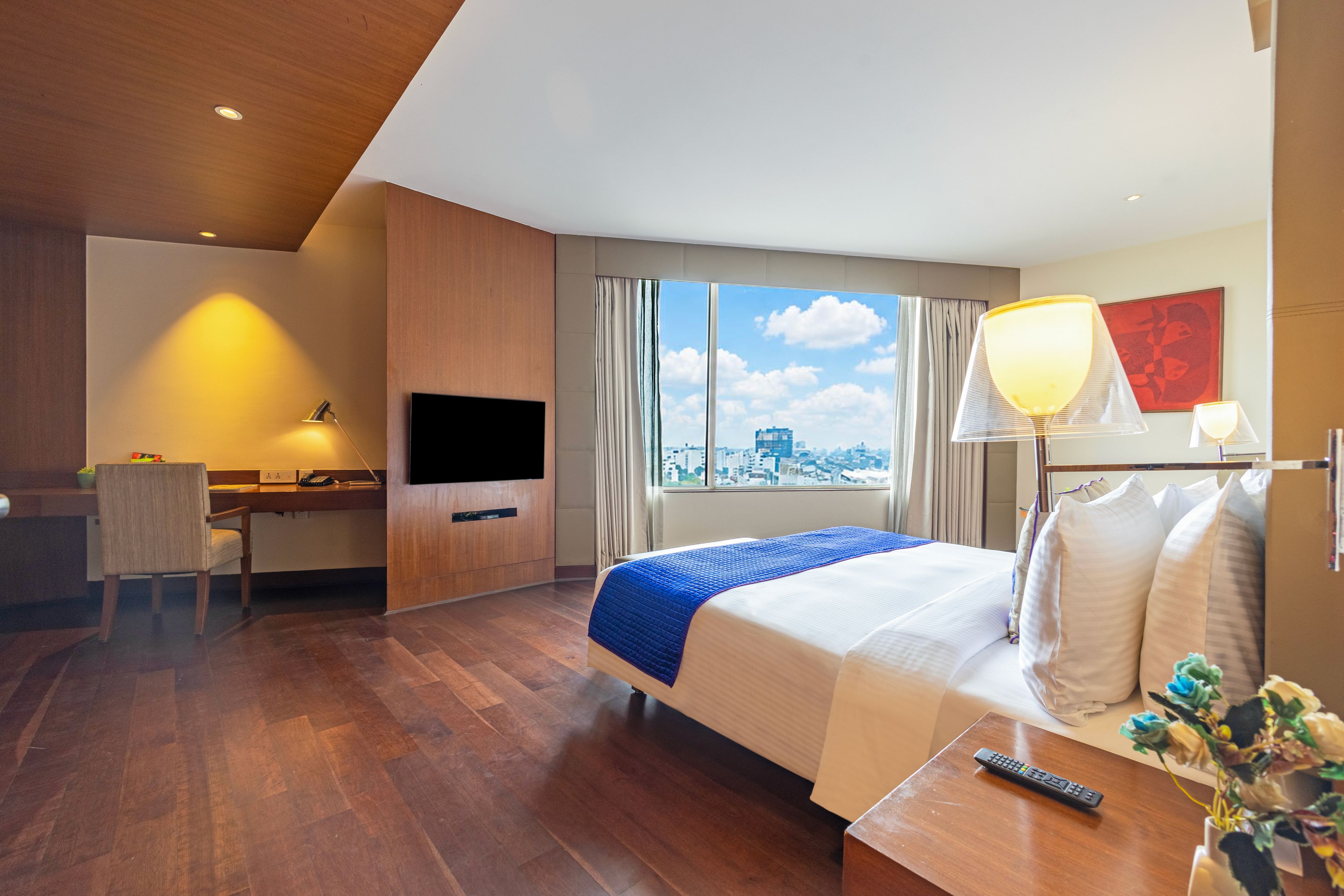 A hotel room with a bed, a desk, a TV, and a view of the city.