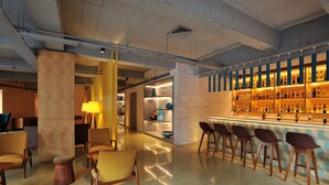 A modern bar area with a brick wall, wooden bar stools, and a well-lit shelf of bottles. - The Anya Hotel, Gurgaon (Gurugram)