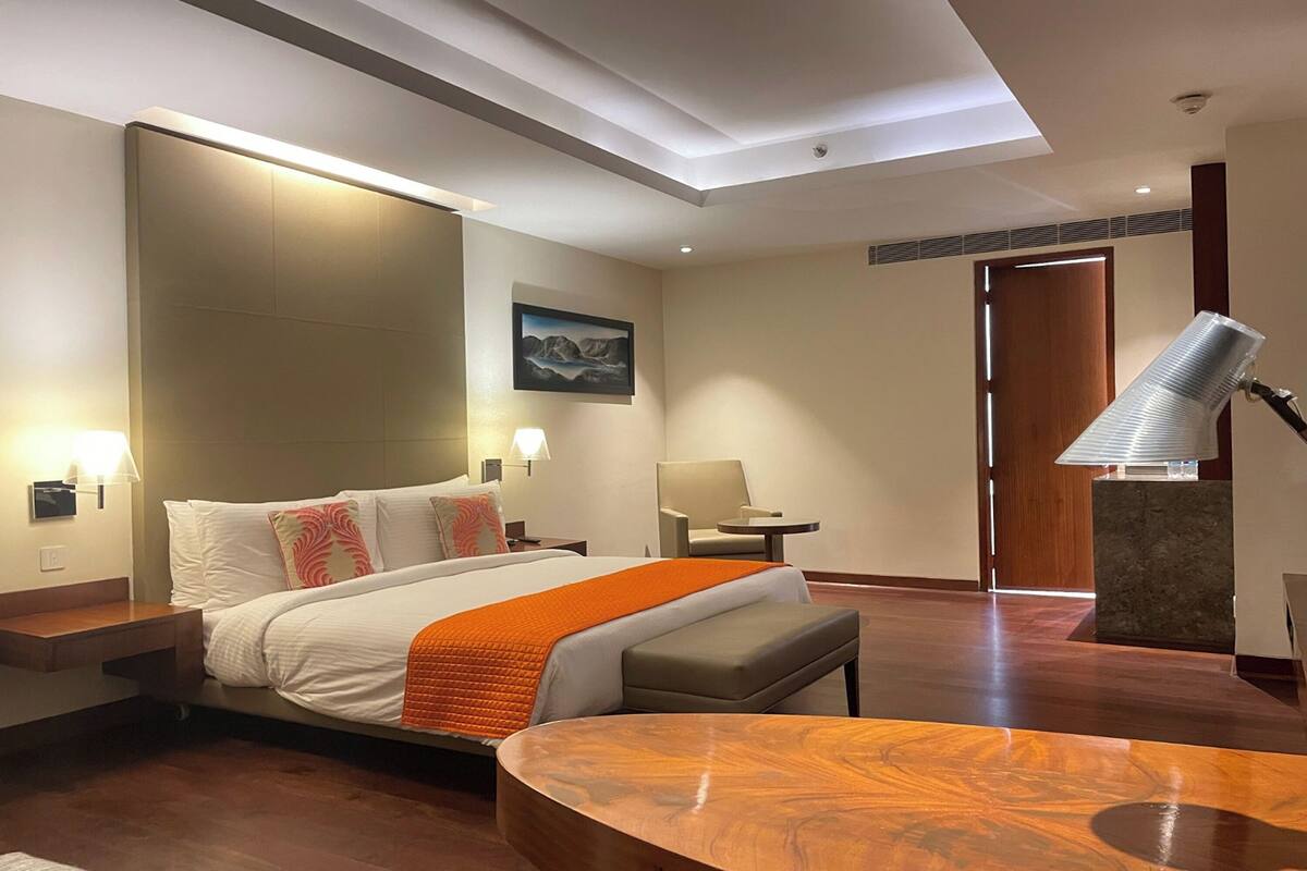 A hotel room with a large bed, a wooden table, a bench, a desk, and a chair.