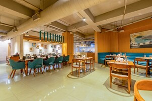 A modern restaurant interior with high ceilings, exposed ductwork, and a mix of seating arrangements including tables and booths.