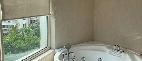 Un baño en esquina con una bañera grande, una ventana con vistas a zonas verdes y un ventilador de techo.