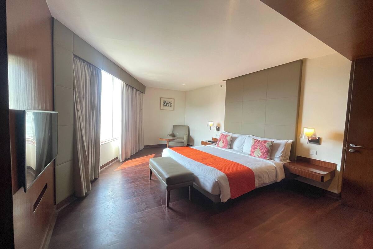 A hotel room with a large bed, a bedside table, a chair, a TV, and a window with curtains.