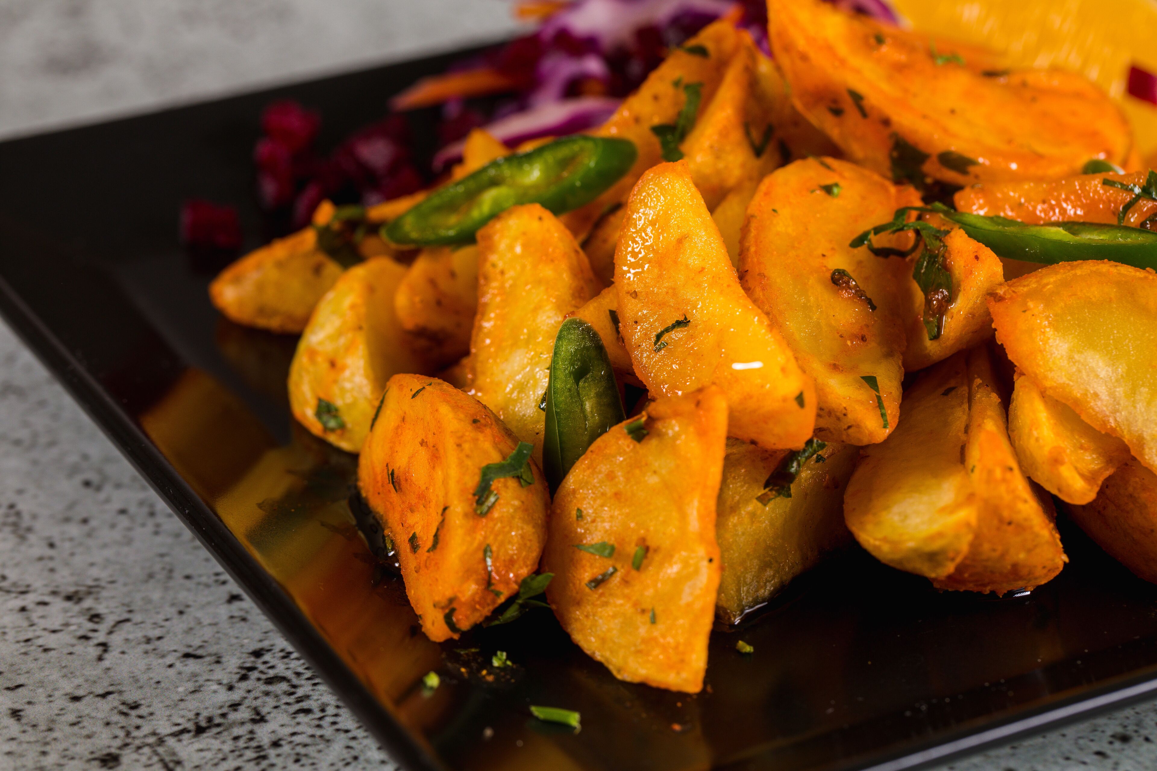 A dish of roasted potatoes garnished with herbs and green chilies.