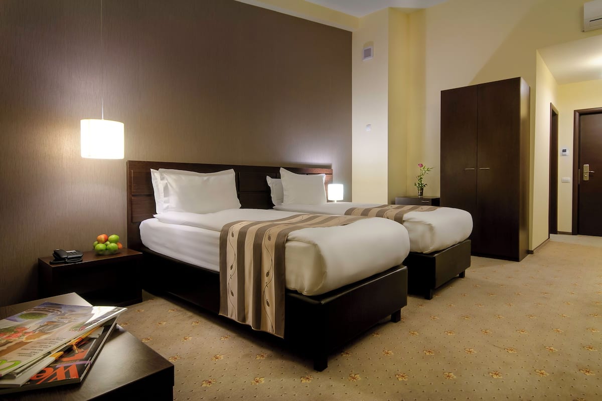 A hotel room with two beds, a nightstand with a phone and fruit, a magazine on a table, and a wardrobe.