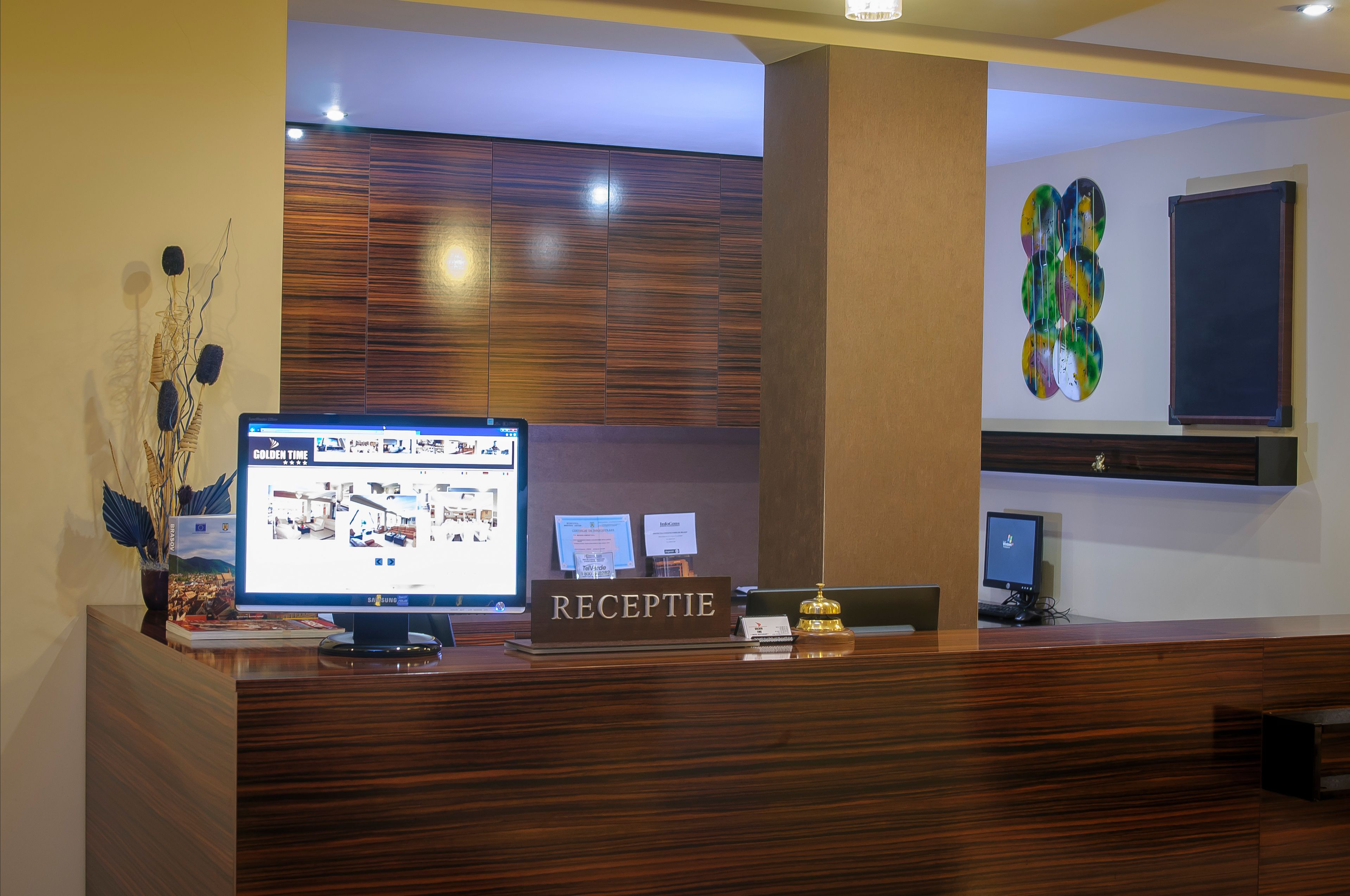 Una recepción con un monitor de computadora mostrando un anuncio de propiedad, un letrero que dice "RECEPTION" y una planta decorativa.